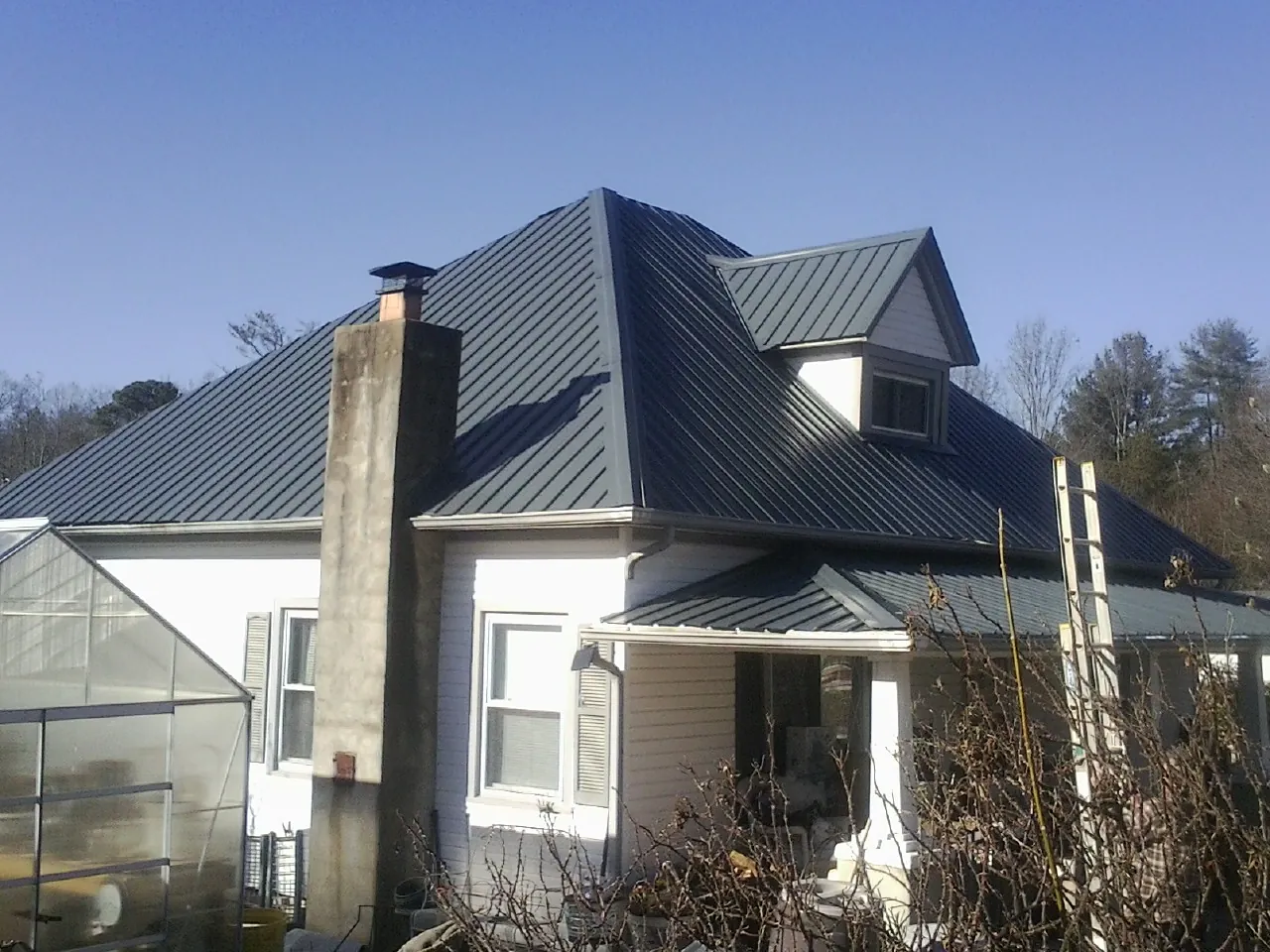 Dark blue standing seam metal roof on a white farmhouse with dormer — Slate & Tile Roof Repair by Roofing Brothers in Saint Johns