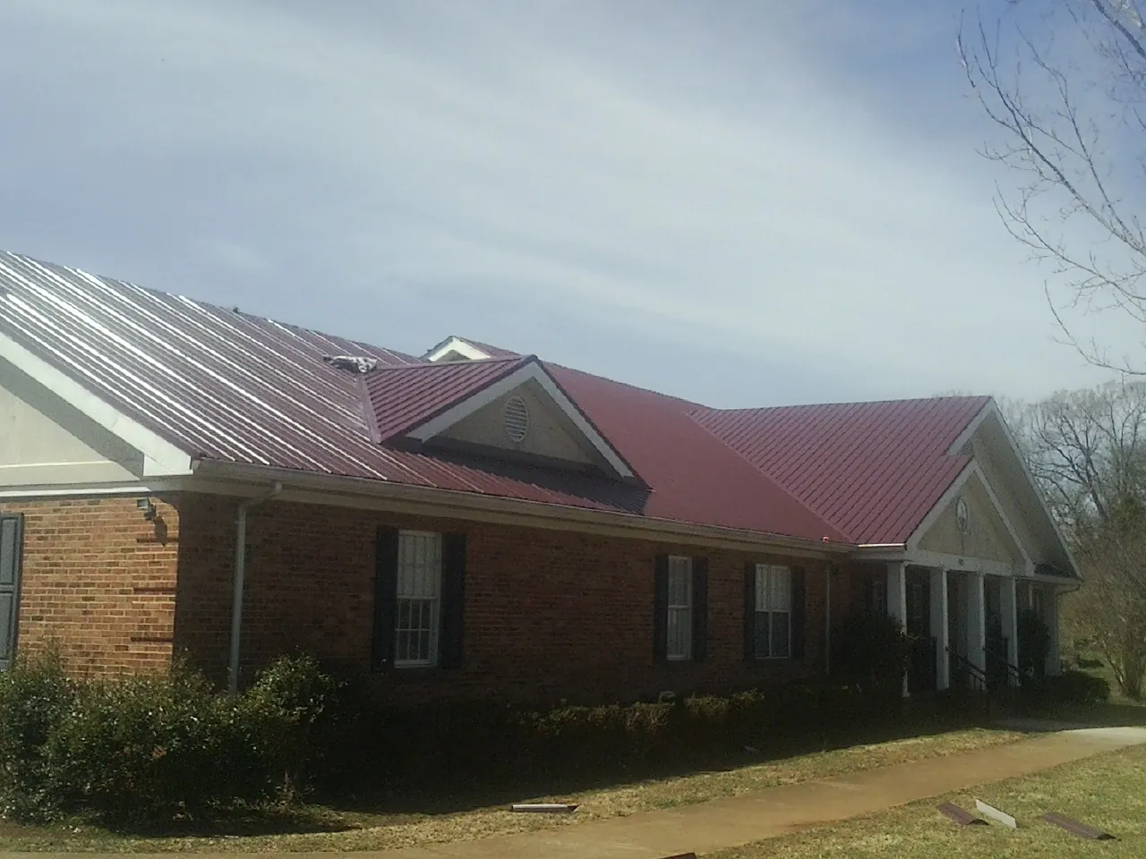 Red metal roof with gabled entries on a long brick building, from a Hail Damage Roof Repair job in Saint Johns