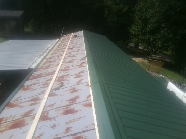 Old rusted panels beside newly installed green metal roofing — Wind Damage Roof Repair by Roofing Brothers in Saint Johns