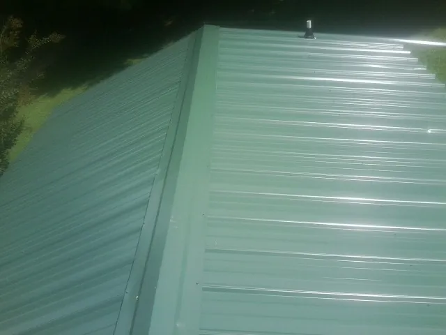 New green metal panels meeting at the ridge of a roof — Flat Roof Repair work by our crew in Saint Johns