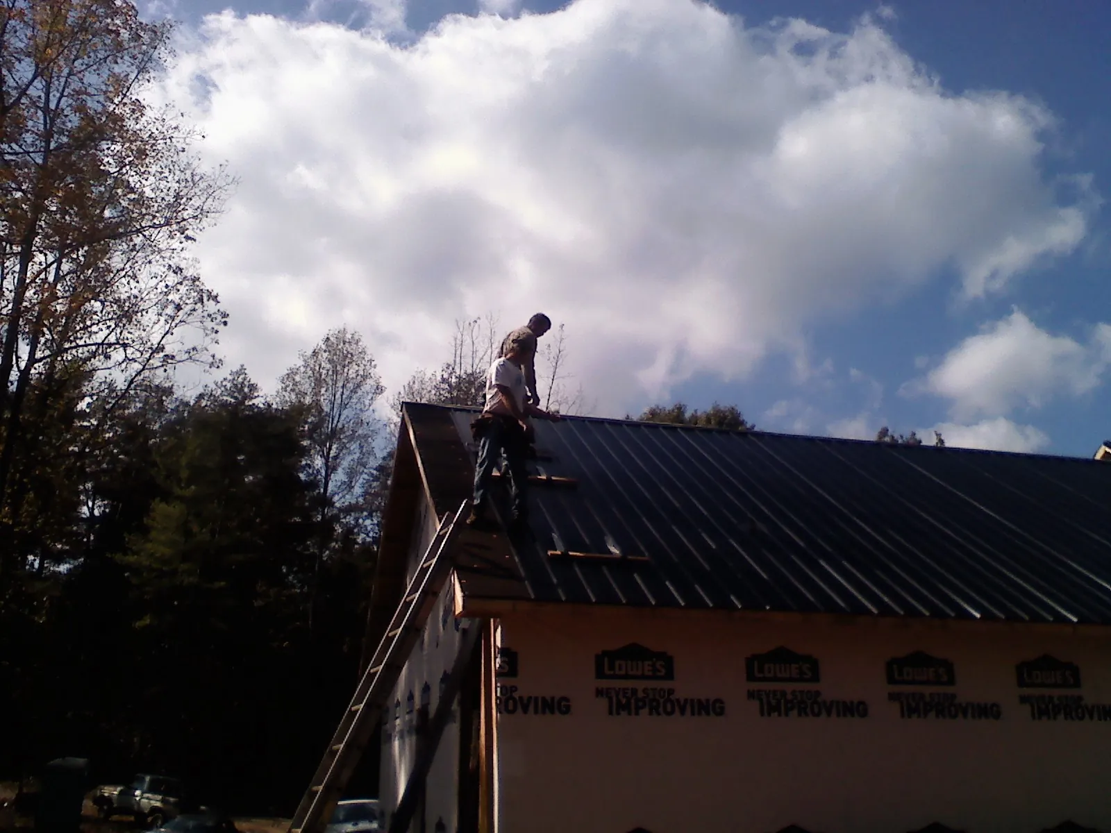 Roofer fastening dark metal panels high against a cloudy sky, from a Roof Inspection job in Saint Johns