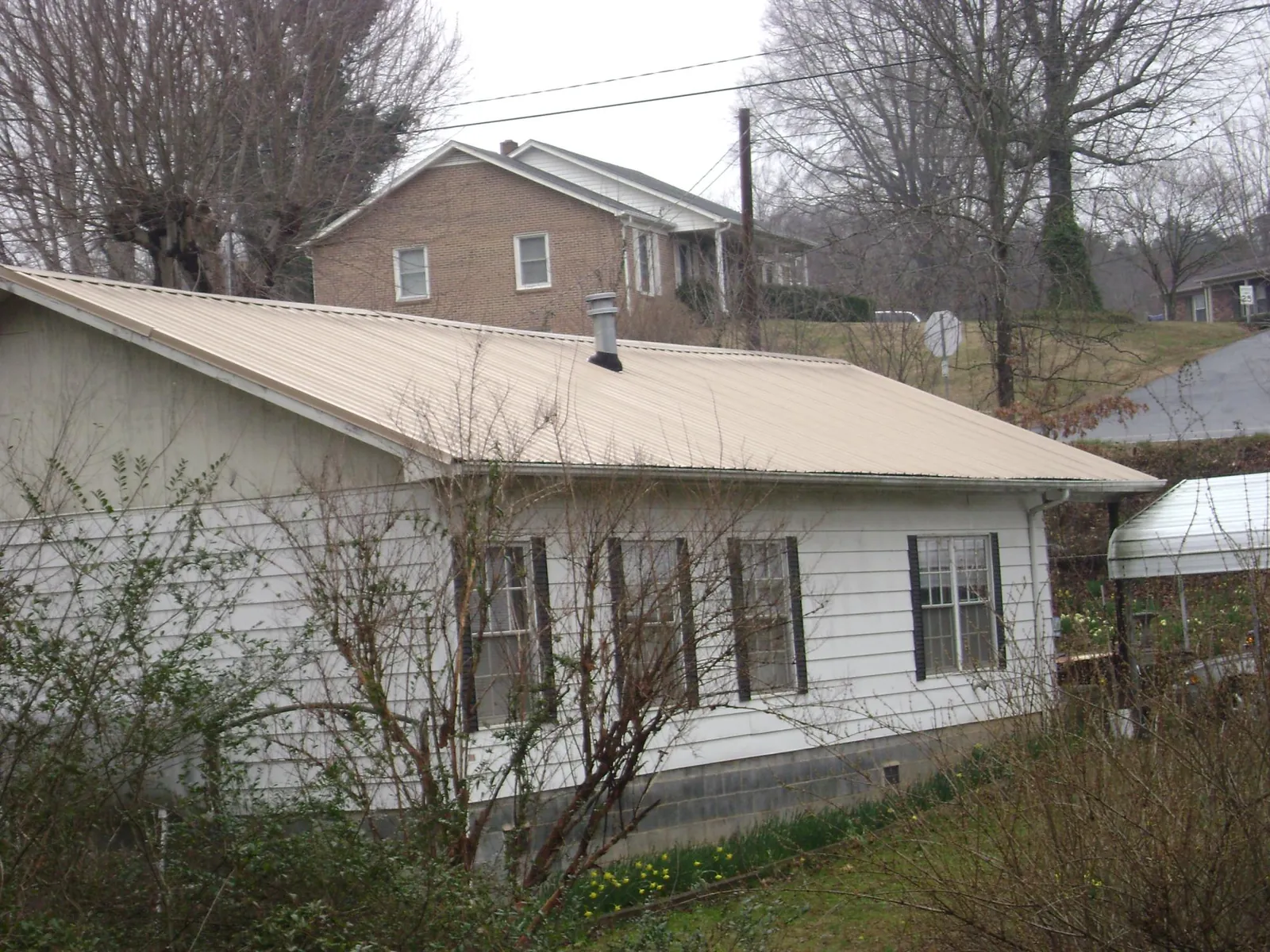 Tan metal roof on a white sided house set into a hillside — Commercial Roofing by Roofing Brothers in Saint Johns