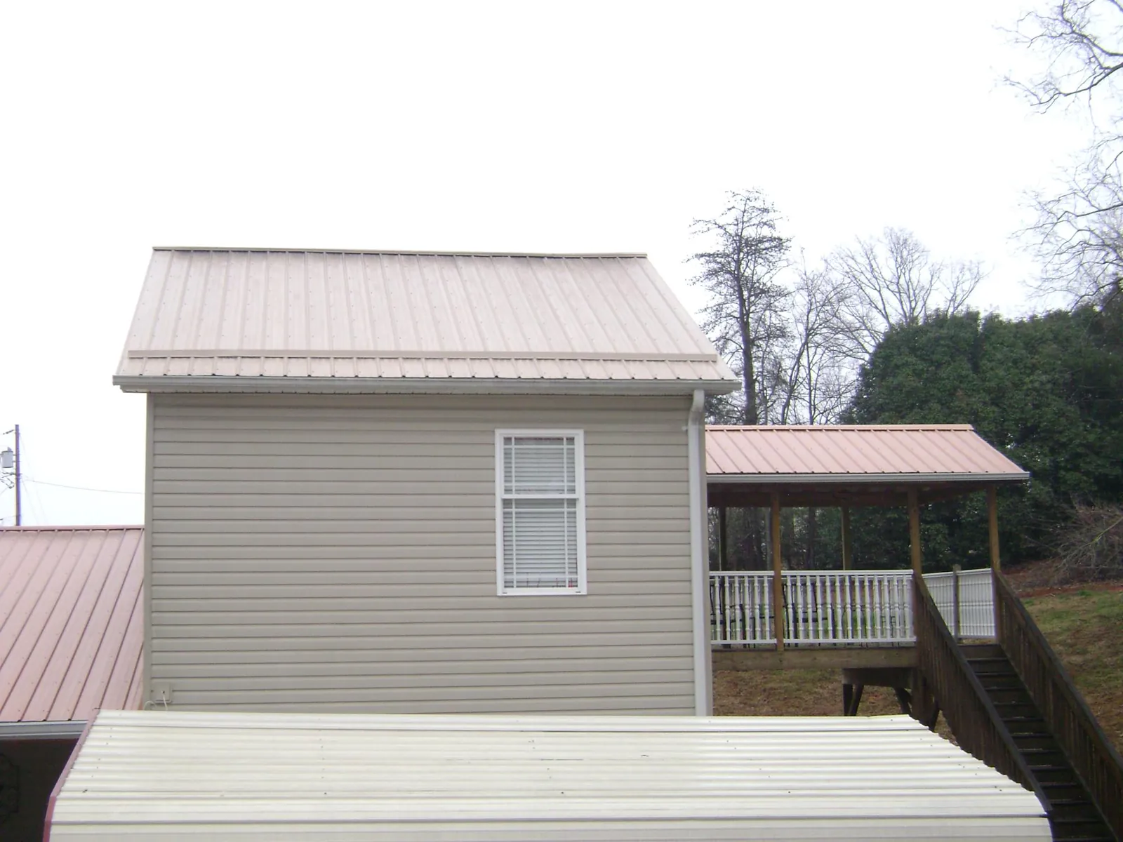 Tan metal roofs on a two story addition and attached porch, from a Roof Replacement job in Saint Johns